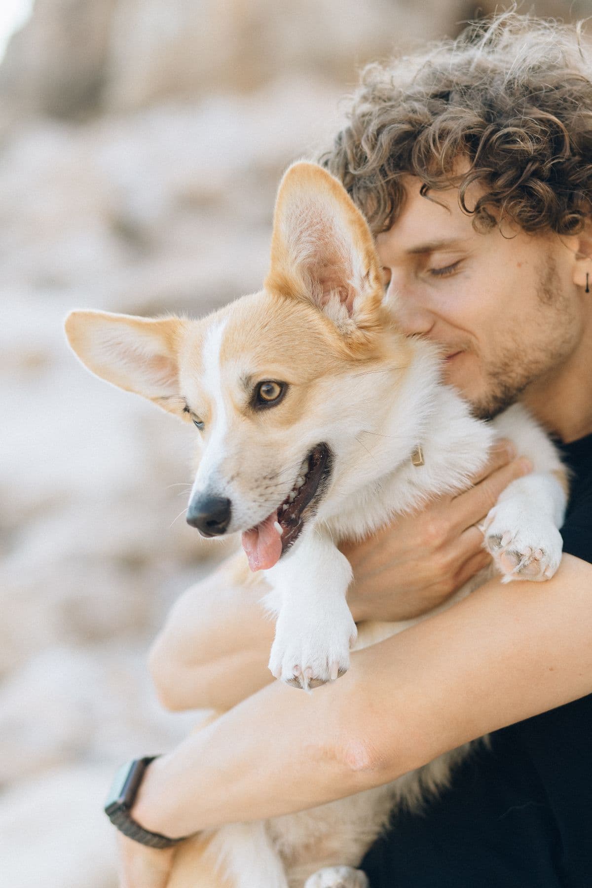 A dog owner holding and nuzzling their happy Corgi outdoors